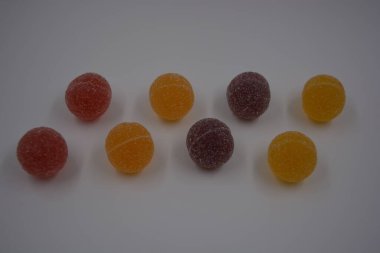 Beyaz şekerle kaplı yuvarlak toplar şeklinde orijinal Finlandiya şekerleri. Sarı, turuncu, kiraz, kırmızı jelibon şekerleri beyaz plastik arka planda bulunur..