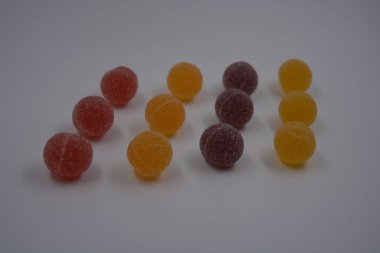 Beyaz şekerle kaplı yuvarlak toplar şeklinde orijinal Finlandiya şekerleri. Sarı, turuncu, kiraz, kırmızı jelibon şekerleri beyaz plastik arka planda bulunur..