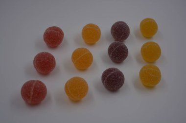 Beyaz şekerle kaplı yuvarlak toplar şeklinde orijinal Finlandiya şekerleri. Sarı, turuncu, kiraz, kırmızı jelibon şekerleri beyaz plastik arka planda bulunur..