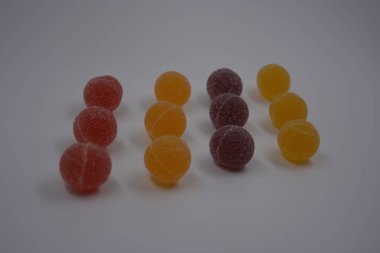 Beyaz şekerle kaplı yuvarlak toplar şeklinde orijinal Finlandiya şekerleri. Sarı, turuncu, kiraz, kırmızı jelibon şekerleri beyaz plastik arka planda bulunur..