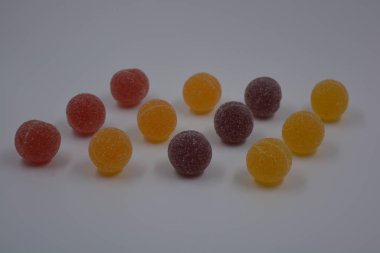 Beyaz şekerle kaplı yuvarlak toplar şeklinde orijinal Finlandiya şekerleri. Sarı, turuncu, kiraz, kırmızı jelibon şekerleri beyaz plastik arka planda bulunur..