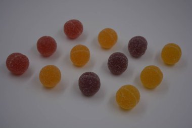 Beyaz şekerle kaplı yuvarlak toplar şeklinde orijinal Finlandiya şekerleri. Sarı, turuncu, kiraz, kırmızı jelibon şekerleri beyaz plastik arka planda bulunur..