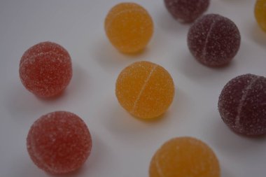 Beyaz şekerle kaplı yuvarlak toplar şeklinde orijinal Finlandiya şekerleri. Sarı, turuncu, kiraz, kırmızı jelibon şekerleri beyaz plastik arka planda bulunur..