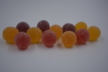 Beyaz şekerle kaplı yuvarlak toplar şeklinde orijinal Finlandiya şekerleri. Sarı, turuncu, kiraz, kırmızı jelibon şekerleri beyaz plastik arka planda bulunur..