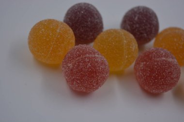 Beyaz şekerle kaplı yuvarlak toplar şeklinde orijinal Finlandiya şekerleri. Sarı, turuncu, kiraz, kırmızı jelibon şekerleri beyaz plastik arka planda bulunur..