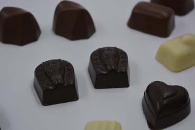 Güzel, alışılmadık ve lezzetli tatlılar, çikolatalar. Beyaz plastik arka planda siyah, süt ve beyaz çikolatadan yapılmış Belçika tatlısı bulunur..