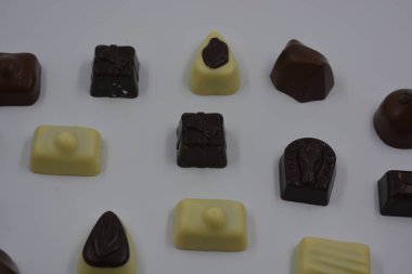 Güzel, alışılmadık ve lezzetli tatlılar, çikolatalar. Beyaz plastik arka planda siyah, süt ve beyaz çikolatadan yapılmış Belçika tatlısı bulunur..