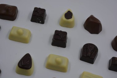 Güzel, alışılmadık ve lezzetli tatlılar, çikolatalar. Beyaz plastik arka planda siyah, süt ve beyaz çikolatadan yapılmış Belçika tatlısı bulunur..