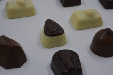 Güzel, alışılmadık ve lezzetli tatlılar, çikolatalar. Beyaz plastik arka planda siyah, süt ve beyaz çikolatadan yapılmış Belçika tatlısı bulunur..