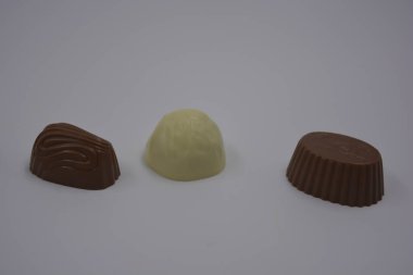 Food, food, very tasty milk candies are located on white plastic. Chocolates are made in the form of leaves, walnuts, medallions, round and square shapes. clipart