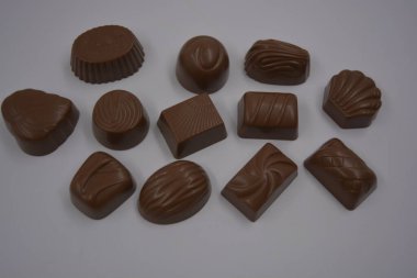 Food, food, very tasty milk candies are located on white plastic. Chocolates are made in the form of leaves, walnuts, medallions, round and square shapes. clipart