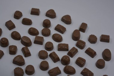 Food, very tasty milk candies are located on white plastic. Chocolates are made in the form of leaves, walnuts, medallions, round and square shapes. clipart