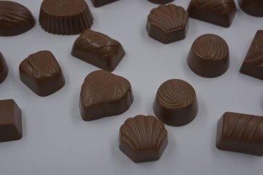 Food, very tasty milk candies are located on white plastic. Chocolates are made in the form of leaves, walnuts, medallions, round and square shapes. clipart