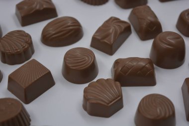 Food, very tasty milk candies are located on white plastic. Chocolates are made in the form of leaves, walnuts, medallions, round and square shapes. clipart