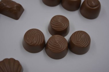 Food, very tasty milk candies are located on white plastic. Chocolates are made in the form of leaves, walnuts, medallions, round and square shapes. clipart