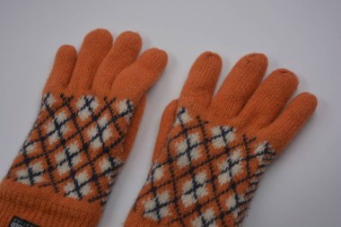 Sıcak, yumuşak, kışlık eşyalar ve ev eşyaları. Güzel turuncu, gri, yalıtılmış, örgü eldivenler beyaz plastik bir arka planda bulunur..