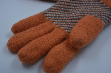 Sıcak, yumuşak, kışlık eşyalar ve ev eşyaları. Güzel turuncu, gri, yalıtılmış, örgü eldivenler beyaz plastik bir arka planda bulunur..