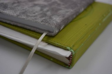 Eşyalar ve objeler, eğitim. Güzel kitaplar, parlak yeşil renkli bir defter, beyaz, boş çarşaflı, beyaz bir kağıt beyaz plastik arka planda yer alır..