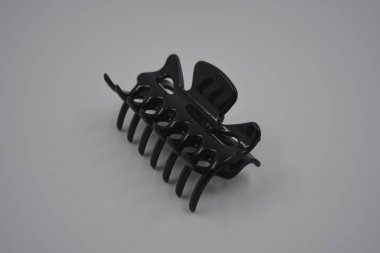 Kadın eşyaları, hayatta sürekli kullanılan nesneler. Siyah plastik takılar, beyaz plastik arka planda sıralanmış kadın saç yengeci..