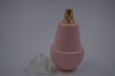Nesneler, eşyalar, kozmetik ürünler ve parfümler. Beyaz plastik arka planda, üzerinde kadın parfümleri, altın sprey ve beyaz bir plastik şapka bulunan güzel, pembe bir şişe bulunur..