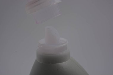 Eşyalar, günlük hayatta kullanılan nesneler. Mor temizlik sıvısıyla dolu büyük plastik bir şişe ve beyaz plastik arka plan üzerine temiz bir plastik kapak yerleştirilir..
