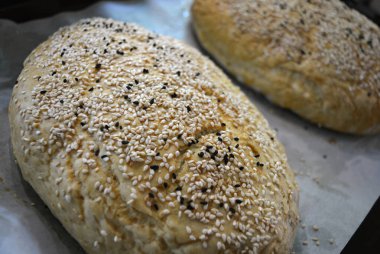 Evde yapılan taze, lezzetli beyaz ekmek. Beyaz ve siyah susam tohumlu iki somun ekmek beyaz parşömen kağıdına konur..