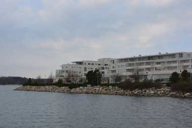 Finlandiya, Espoo 'da körfez ve bahar doğası olan parlak ve renkli manzaralar. Güzel berrak su, sarı kumlu büyük sahil, dalgalar, uzun yeşil çam ağaçları, bahçe ağaçları, büyük taşlar, renkli su deposu, körfez, göl.