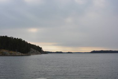 Finlandiya, Espoo 'da körfez ve bahar doğası olan parlak ve renkli manzaralar. Güzel berrak su, sarı kumlu büyük sahil, dalgalar, uzun yeşil çam ağaçları, bahçe ağaçları, büyük taşlar, renkli su deposu, körfez, göl.