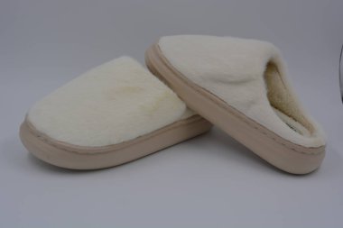 Güzel ve alışılmadık kadın eşyaları, günlük ev ayakkabıları. Kalın kahverengi, bej tabanlı sentetik kürkten yapılmış beyaz yumuşak terlikler beyaz plastik bir arka planda yer almaktadır..