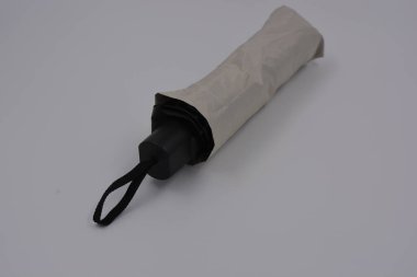 Yeni, güzel bej, altın, beyaz, siyah saplı, açık renk şemsiye, su ve yağmurdan siyah astarlı beyaz plastik arka planda yer almaktadır..