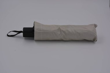 Yeni, güzel bej, altın, beyaz, siyah saplı, açık renk şemsiye, su ve yağmurdan siyah astarlı beyaz plastik arka planda yer almaktadır..