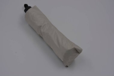 Yeni, güzel bej, altın, beyaz, siyah saplı, açık renk şemsiye, su ve yağmurdan siyah astarlı beyaz plastik arka planda yer almaktadır..