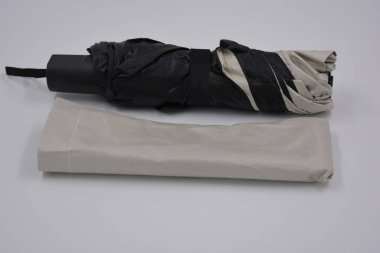 Yeni, güzel bej, altın, beyaz, siyah saplı, açık renk şemsiye, su ve yağmurdan siyah astarlı beyaz plastik arka planda yer almaktadır..
