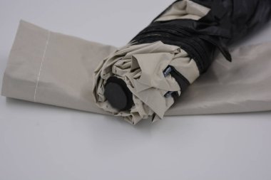 Yeni, güzel bej, altın, beyaz, siyah saplı, açık renk şemsiye, su ve yağmurdan siyah astarlı beyaz plastik arka planda yer almaktadır..