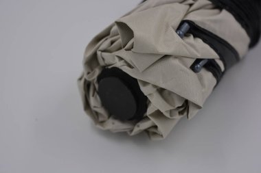 Yeni, güzel bej, altın, beyaz, siyah saplı, açık renk şemsiye, su ve yağmurdan siyah astarlı beyaz plastik arka planda yer almaktadır..