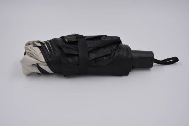 Yeni, güzel bej, altın, beyaz, siyah saplı, açık renk şemsiye, su ve yağmurdan siyah astarlı beyaz plastik arka planda yer almaktadır..