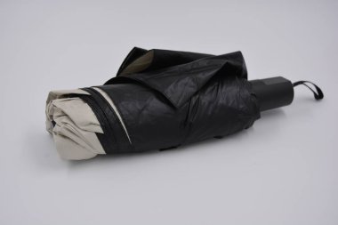 Yeni, güzel bej, altın, beyaz, siyah saplı, açık renk şemsiye, su ve yağmurdan siyah astarlı beyaz plastik arka planda yer almaktadır..