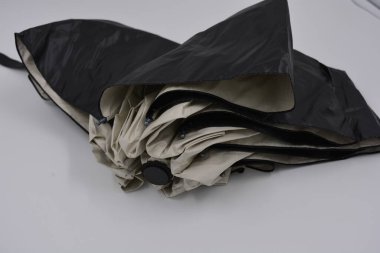 Yeni, güzel bej, altın, beyaz, siyah saplı, açık renk şemsiye, su ve yağmurdan siyah astarlı beyaz plastik arka planda yer almaktadır..