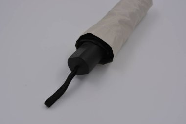 Yeni, güzel bej, altın, beyaz, siyah saplı, açık renk şemsiye, su ve yağmurdan siyah astarlı beyaz plastik arka planda yer almaktadır..