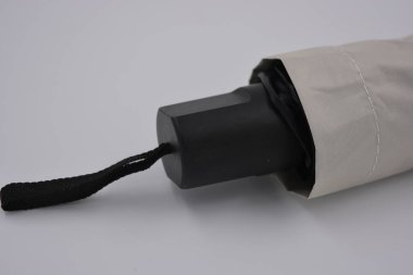 Yeni, güzel bej, altın, beyaz, siyah saplı, açık renk şemsiye, su ve yağmurdan siyah astarlı beyaz plastik arka planda yer almaktadır..