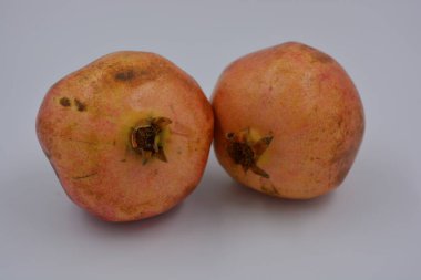 Ürünler, sağlıklı ve sağlıklı yiyecekler, taze meyveler. Olgun sulu iki kırmızı-kahverengi nar beyaz bir plastik arka planda yer alır..