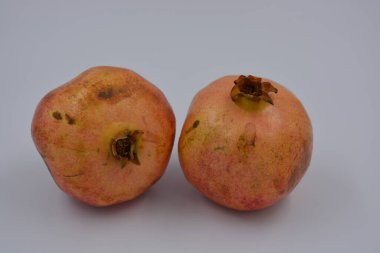 Ürünler, sağlıklı ve sağlıklı yiyecekler, taze meyveler. Olgun sulu iki kırmızı-kahverengi nar beyaz bir plastik arka planda yer alır..