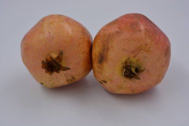 Ürünler, sağlıklı ve sağlıklı yiyecekler, taze meyveler. Olgun sulu iki kırmızı-kahverengi nar beyaz bir plastik arka planda yer alır..