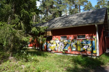 Finlandiya, Espoo 'daki Hyljelahti bölgesinin güzel ve canlı doğası. Uzun köknar ağaçları, süsleri, kumlu bir yolun yakınındaki eski kırmızı ahşap evi olan geçilemez yeşil orman..