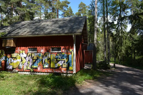 Finlandiya, Espoo 'daki Hyljelahti bölgesinin güzel ve canlı doğası. Uzun köknar ağaçları, süsleri, kumlu bir yolun yakınındaki eski kırmızı ahşap evi olan geçilemez yeşil orman..