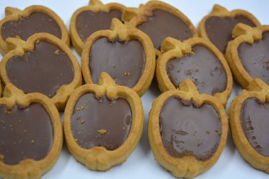 İçinde fındıklı, çikolatalı kurabiyeler olan taze, lezzetli çıtır kurabiyeler. Beyaz bir arka planda kahverengi dolgulu elma şekilli kurabiyeler.