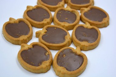 İçinde fındıklı, çikolatalı kurabiyeler olan taze, lezzetli çıtır kurabiyeler. Beyaz bir arka planda kahverengi dolgulu elma şekilli kurabiyeler.