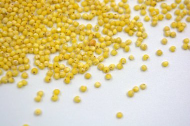 Çok sağlıklı ve kullanışlı homurtular, beyaz bir arka plana saçılmış sarı darılar. Bu mısır gevreğindeki yulaf lapası vücuttaki toksinleri temizler..