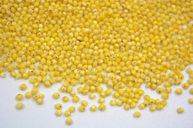 Çok sağlıklı ve kullanışlı homurtular, beyaz bir arka plana saçılmış sarı darılar. Bu mısır gevreğindeki yulaf lapası vücuttaki toksinleri temizler..