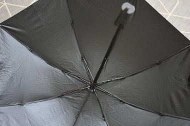 Günlük nesneler. Siyah astarlı açık gri bej şemsiye bej ahşap zeminde duruyor..